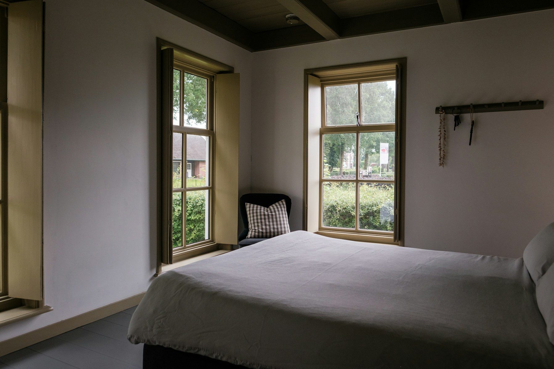 A bedroom with two tall casement windows and dark ceiling beams.