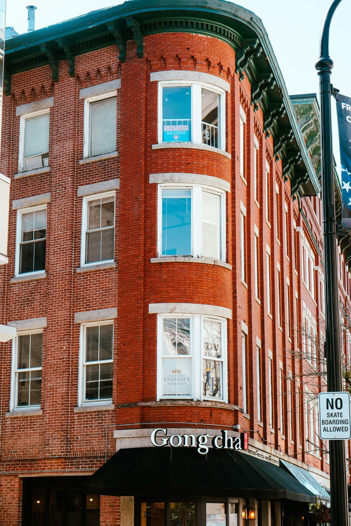 A four-story red brick building with stacked bay windows on a downtown street corner.