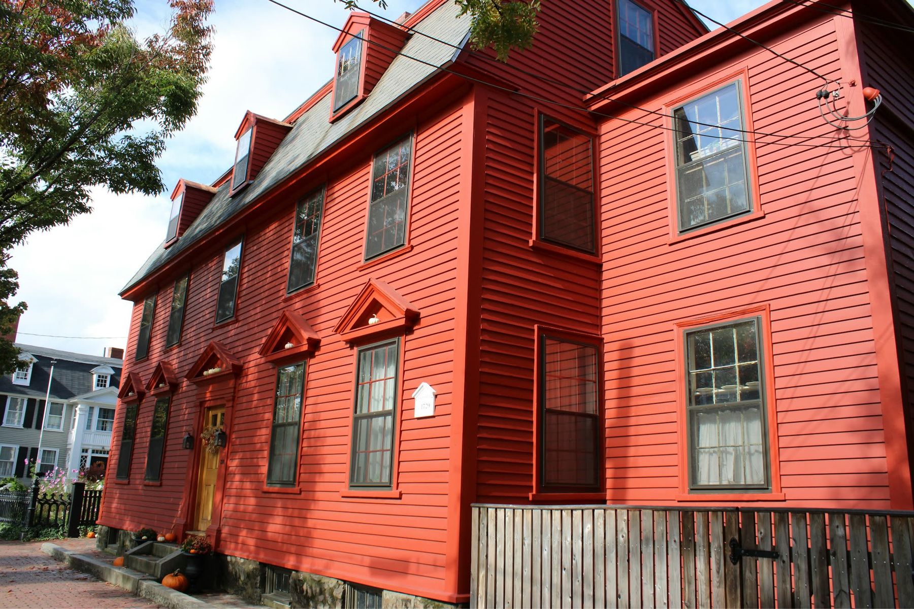 A barn-red clapboard colonial with pedimented window heads and dormers, above a brick sidewalk.