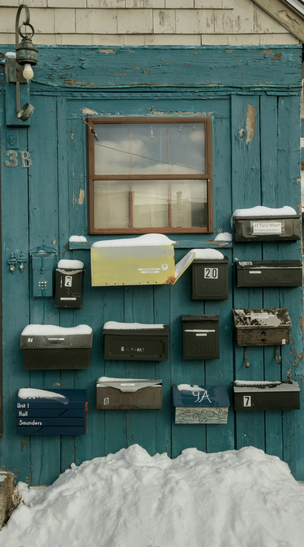 Rows of weathered mailboxes on a faded teal door, snow banked against the bottom.