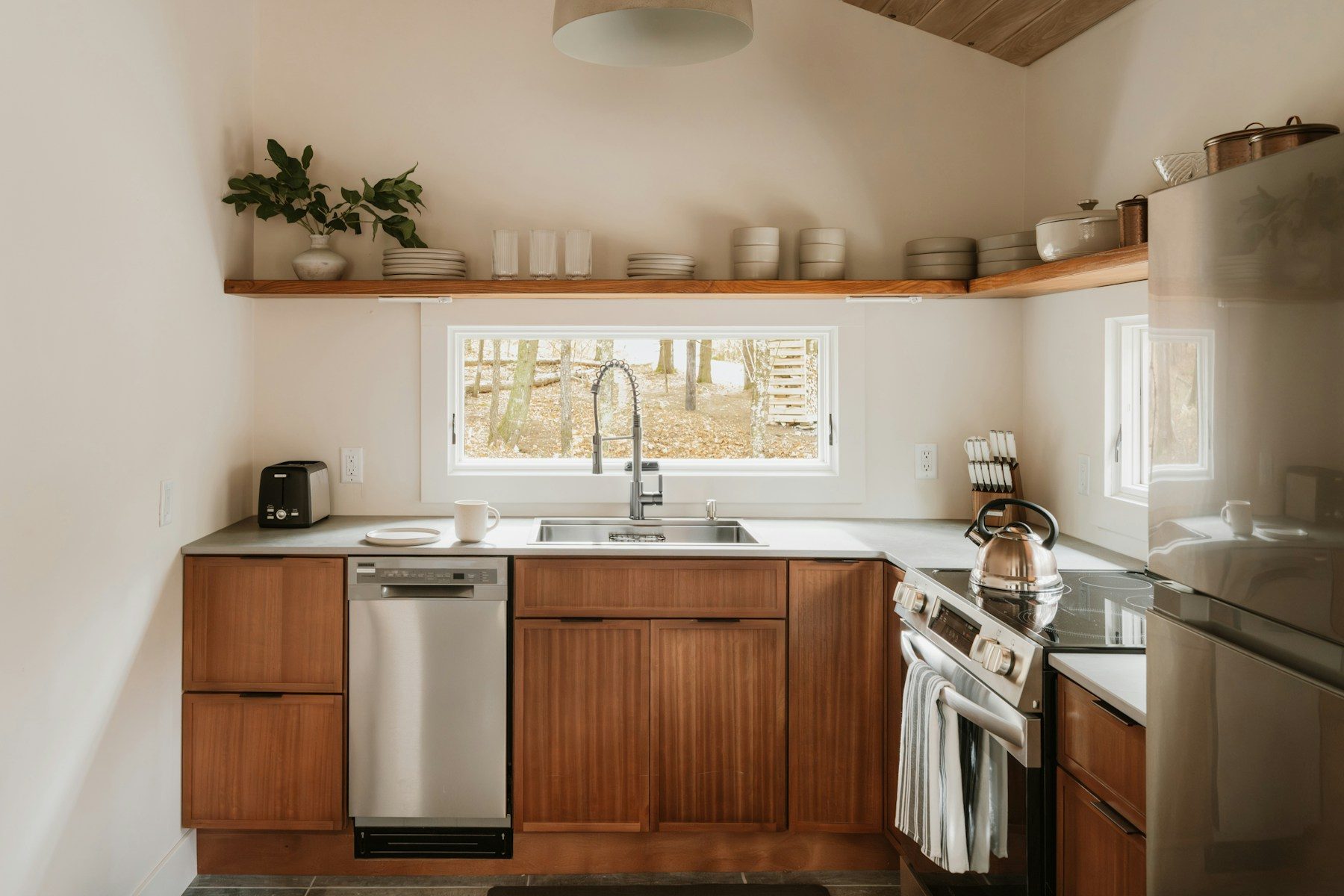 A kitchen with wood lower cabinets, open shelving and a wide window over the sink.