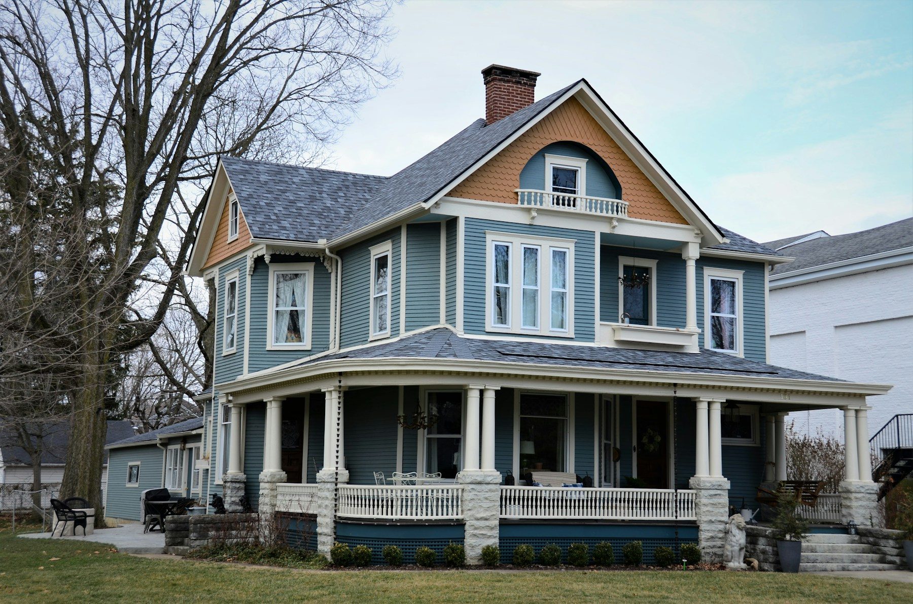 A blue Queen Anne house with white trim, a turned-post wraparound porch and a decorated front gable.