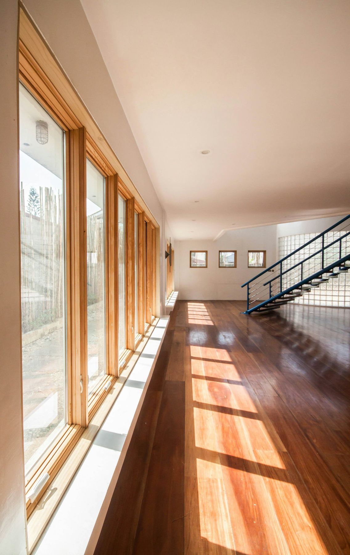 A long, bright corridor of tall windows throwing bars of sunlight across a wide-plank wood floor.
