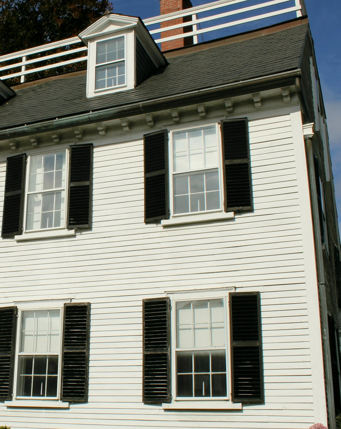 A white clapboard house with black shutters and a slate roof, cropped tall.